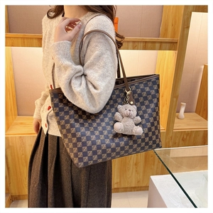 Detail view of large brown monogram tote bag with a cute plush bear charm on the strap