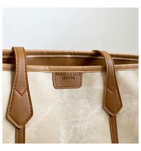 Detailed close-up of beige canvas tote bag with brown leather handles and fine stitching
