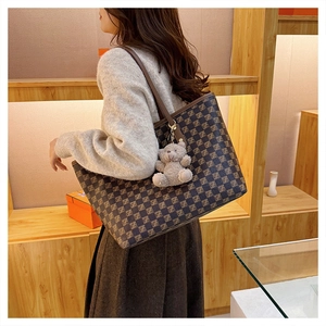 Brown checkered tote bag with leather handles and teddy bear charm shown on shoulder