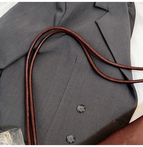 Detail of dark brown leather shoulder strap paired with a grey double-breasted suit