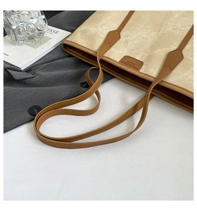 Detail of canvas tote bag with brown leather handles and brand tag on a neutral background