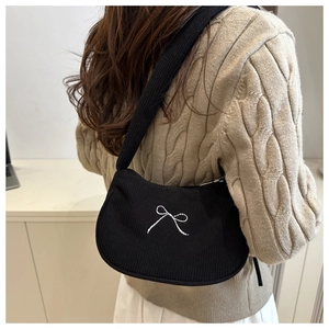 Close-up of black knitted shoulder bag with white bow embroidery and ribbed texture