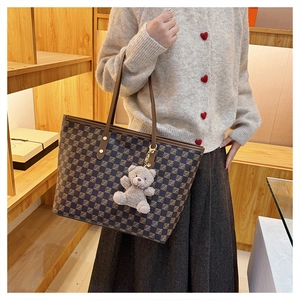 Close-up of checkered tote bag with brown leather handles and a plush teddy bear charm