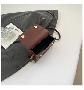 Detailed shot of a red-brown leather crossbody bag with golden magnetic snap closure