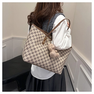 Detail of a large monogram tote bag with brown leather trim and a plush bear charm