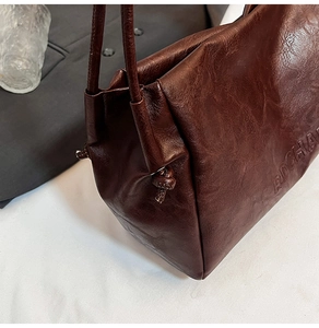 Detail of dark brown tote bag showing pleated leather texture and embossed logo accents