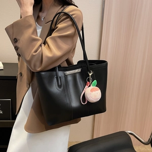 Classic black tote bag with peach plush charm shown on a stylish urban model
