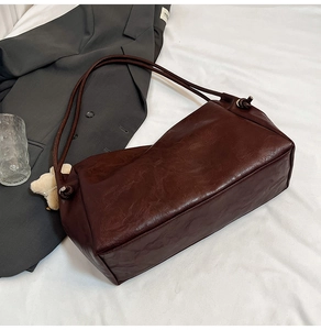 Detailed texture of dark brown PU leather tote bag with white plush bear charm accessory