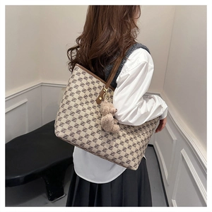 Detail of a large monogram tote bag with brown leather straps and a plush bear charm