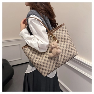 Detail of a large monogram tote bag with brown leather handles and a cute teddy bear charm