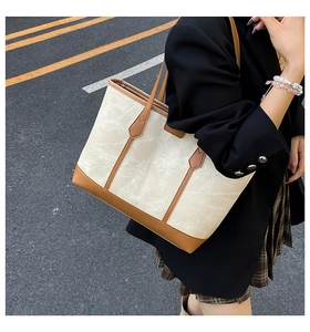 Canvas tote bag with brown leather trim carried by a model on a sunny outdoor street