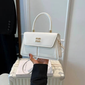 Elegant white square handbag with gold logo on a vintage suitcase in a bright room