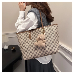 Detail of printed tote bag featuring a teddy bear charm and brown leather straps