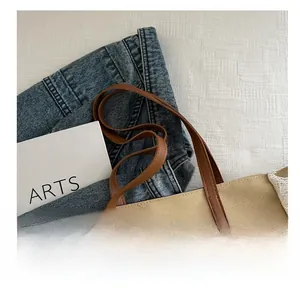 Détail du cabas en toile kaki avec bords frangés et poignées en cuir marron sur tissu