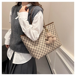 Detail of beige printed tote bag with brown leather straps and a plush bear pendant