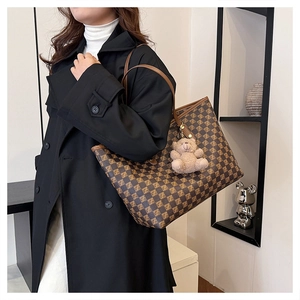 Macro detail of checkered tote bag with plush bear charm worn with a black coat
