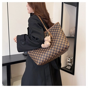 Detail of checkered tote bag side view with brown leather handle and cute plush bear charm