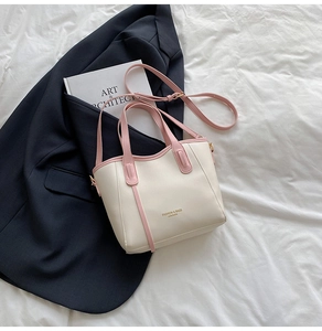 Close-up of cream and pink leather bucket bag with gold hardware on white fabric
