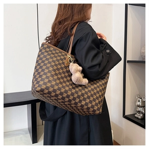 Classic patterned tote bag with brown leather handles and a plush bear charm detail