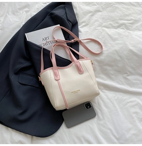 Top view of cream bucket bag with pink straps on a bed next to a blue blazer