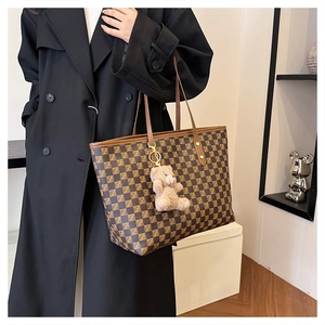 Close-up of brown checkered tote bag with gold rivets and cute plush bear charm accessory