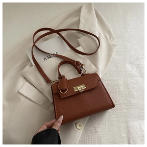 Detail of dark brown lychee textured handbag with golden metal twist lock and top handle