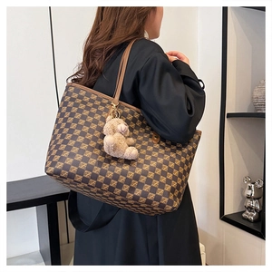 Side view of large checkerboard tote bag with bear charm worn by a model