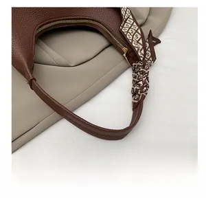 Detail einer braunen Handtasche aus Leder mit Seidenschal und goldenem Reißverschluss