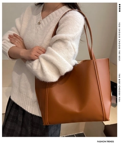 Brown leather tote bag shown on shoulder featuring vertical stripes and spacious design