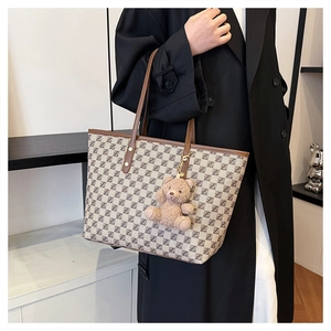 Detail of vintage patterned tote bag with brown leather handles and plush bear charm