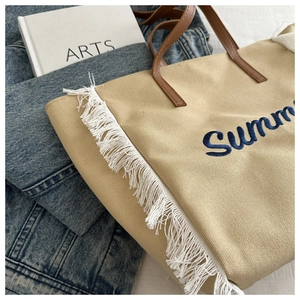 Gros plan d'un sac cabas en toile beige avec broderie Summer bleue et bordures à franges