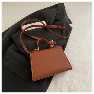 Brown lychee-textured trapezoid handbag with gold hardware on a stylish suit blazer