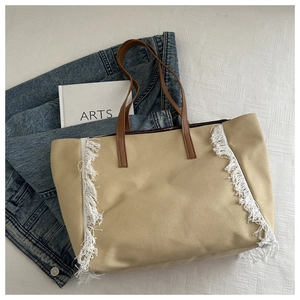 Détail d'un sac cabas beige avec franges blanches et poignées en similicuir marron