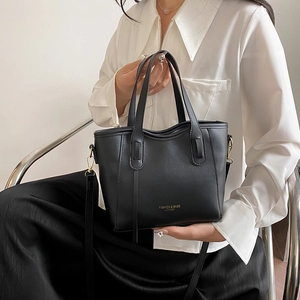 Minimalist black leather bucket bag with top handles and gold text shown on a model