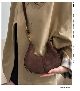 Detail shot of brown suede crescent bag with gold hardware on a khaki coat