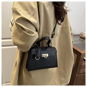 Detail of black lychee grain leather handbag with gold metal clasp on a trench coat
