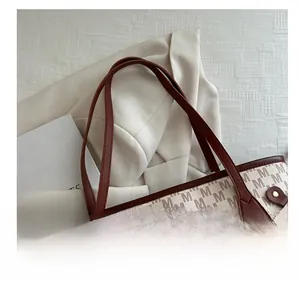 Close-up of leather handle and monogram print on large capacity tote bag with rivets