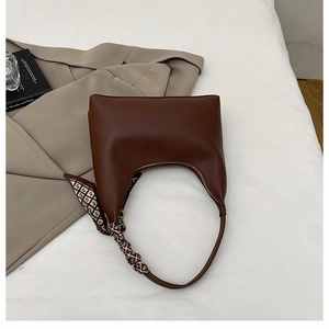 Close-up of brown lychee grain leather handbag with gold zipper and decorative silk scarf