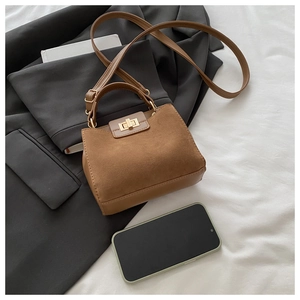 Detail of a brown textured handbag with gold lock on a white fabric background