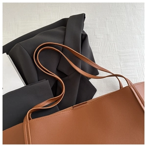Detail of minimalist brown leather tote bag with slim shoulder straps on white texture