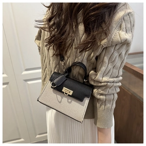 Detail of elegant beige canvas crossbody bag with black leather trim and gold twist lock