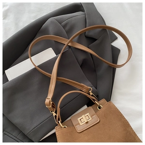 Detail of brown suede tote bag with golden twist lock on grey blazer suit background