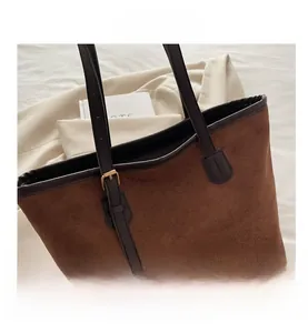 Détail du sac cabas en daim marron avec anses en cuir foncé et boucles en métal doré