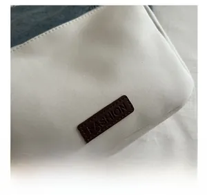 Détail du tissu en toile blanche imperméable avec écusson de mode en cuir marron