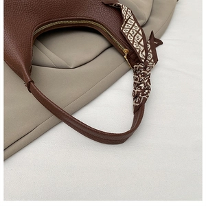Detail of a brown hobo bag showing litchi leather texture and decorative silk scarf