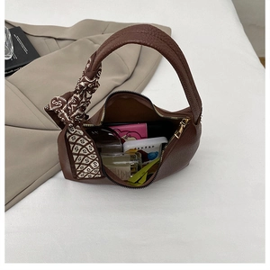 Macro detail of brown lychee texture handbag with a decorative silk scarf and zip closure