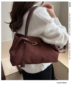 Detail of dark brown suede tote bag with slim shoulder strap worn on a white sweater