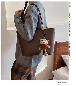 Detail of dark brown tote bag with plush bear charm and slender shoulder straps