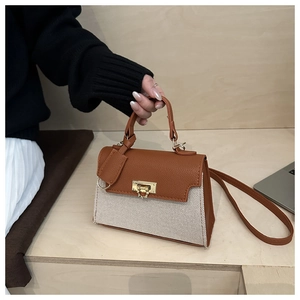 Detail of a brown leather and beige canvas crossbody bag with a gold twist lock clasp