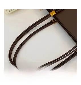Detail view of brown leather tote bag showing handle stitches and gold hardware